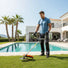 Athletic man trimming grass around luxury villa pool in south of France with GX3G 35cc 4-stroke gas trimmer-minisawpro