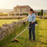 Woman trimming grass around stone fence on French countryside farm with S680 52cc gas lawn trimme-minisawpro