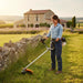 Woman trimming grass around stone fence on French countryside farm with S680 52cc gas lawn trimme-minisawpro