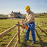 Construction worker trimming fence posts at rural farmhouse renovation with MIP2J00 25.4cc petrol chainsaw-minisawpro