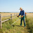 Man clearing tall weeds along wooden fence with MIP1399 quiet 4-stroke gas grass trimmer – portable lawn tool-minisawpro
